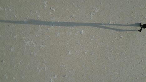 Langer-Schatten-Einer-Person-Oder-Silhouette,-Die-Auf-Der-Oberfläche-Eines-Ausgetrockneten-Salzsees-Läuft