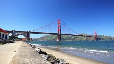 Das-Wahrzeichen-Der-Golden-Gate-Bridge-In-Leuchtendem-Rot-Vor-Blauem-Himmel-Entlang-Der-Promenade-Und-Dem-Strand,-San-Francisco,-USA