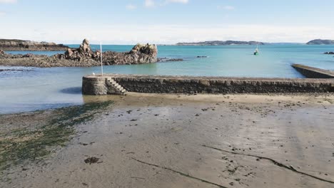 Bordeaux-Harbour-Guernsey-low-drone-footage-from-shore-towards-harbour-wall-on-sunny-day-with-Herm-and-Jethou-in-the-background