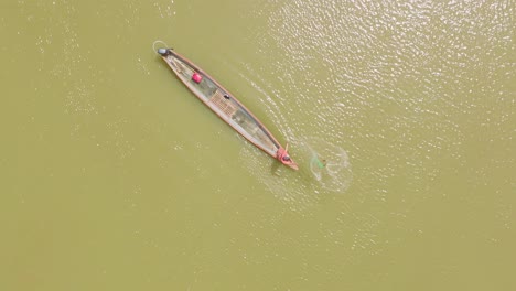 A-longboat-sailing-on-the-green-waters-of-florencia,,-man-fishing-colombia,-aerial-view