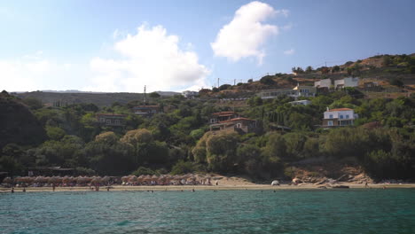 Una-Serena-Escena-De-Playa-Con-Gente-Relajándose-Y-Nadando,-Frente-A-Colinas-Verdes-Y-Un-Cielo-Despejado