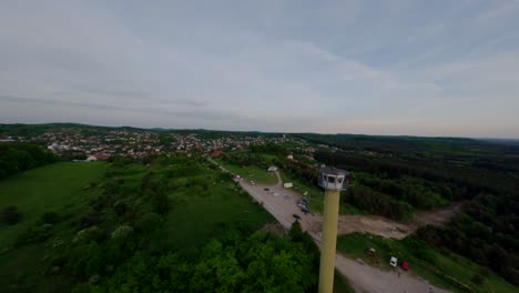 Hoher-Wachturm-In-Der-Nähe-Der-Stadt-Und-Waldlandschaft,-Luftaufnahme-Der-FPV-Umlaufbahn