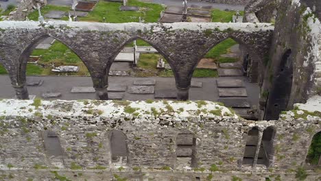 Altos-Arcos-De-Piedra-De-Ruinas-Desmoronadas-En-El-Convento-De-Claregalway-Cubiertos-De-Musgo,-Panorámica-Aérea-De-Alto-ángulo