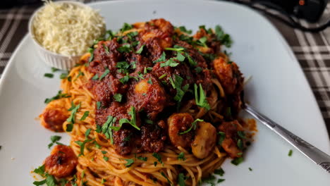 A-plate-filled-with-spaghetti-and-seafood-in-tomato-sauce,-grated-cheese-on-the-side