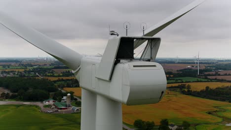 Turbina-Eólica-Desde-Atrás-Con-Un-Dron-Aéreo-Cerca-De-Una-Toma-Orbital-Panorámica-Con-Tierras-De-Cultivo-En-El-Fondo