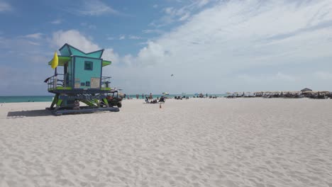 Wide-shot-of-Miami-Beach-with-white-sand,-people-relaxing,-and-buildings-in-the-background