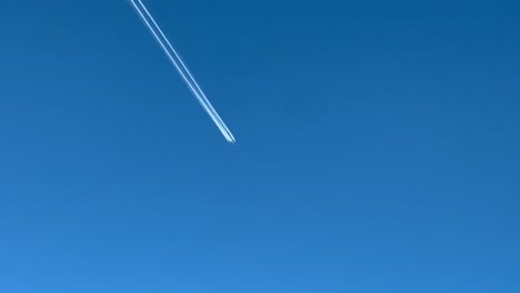 Contrail-of-a-huge-military-4-engine-aircraft-crossing-a-blue-sky,-shot-from-an-airplane-flying-bellow