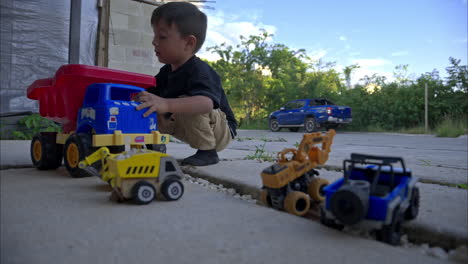 Slow-motion-panning-of-a-young-mexican-latin-boy-playing-with-his-toy-trucks-on-his-house-driveway-in-the-afternoon