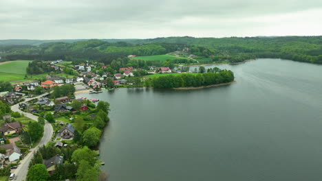 Aerial-view-of-Ostrzyce-village-by-a-lake,-surrounded-by-lush-green-hills-and-forests
