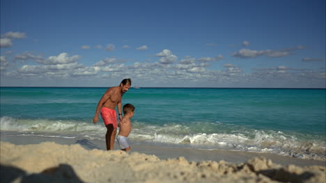 Slow-motion-of-a-mexican-latin-fit-daddy-playing-with-his-son-running-away-from-the-water-towards-the-camera-smiling-laughing-and-having-fun