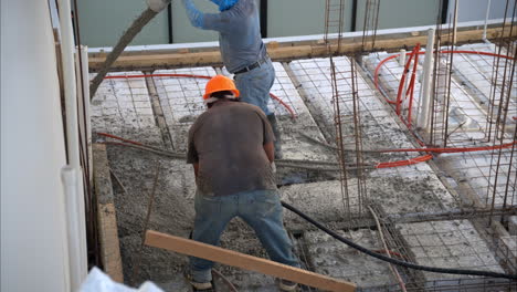 Slow-motion-of-a-pair-of-mexican-latin-workers-applying-fresh-concrete-from-a-boom-pump-on-grid-structure-to-make-the-slab-of-a-house-in-Mexico
