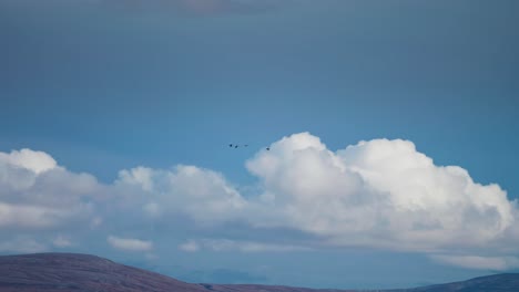 A-small-flock-of-birds-flies-fast-above-the-mountainous-landscape-and-clouds-in-the-background