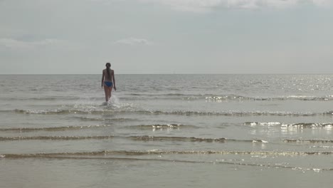 Walking-against-incoming-tide-slow-motion,-teenage-girl,-sunrise-scene