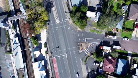 Landscape-drone-aerial-of-main-road-set-of-traffic-lights-cars-driving-in-small-town-street-suburbs-next-to-train-station-Ourimbah-Australia-transport-travel