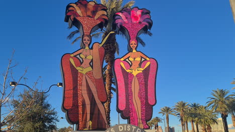 Las-Vegas,-USA,-Artis-District-Schild-Mit-Großer-Showgirls-Installation-An-Einem-Sonnigen-Abend