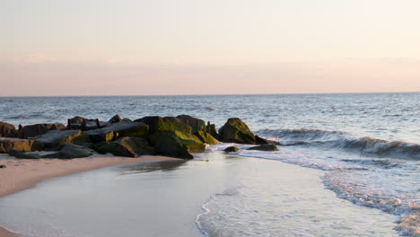 Waves-Splash-Against-Emerald-Green-Mossy-Rocks-and-Wash-Ashore-on-Clear-Evening-in-Slow-Motion