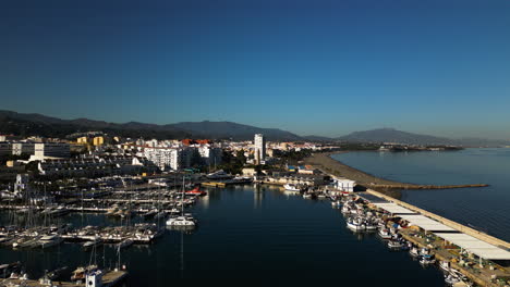 Yachts-moored-in-pier-of-Estepona-and-cityscape-view,-aerial