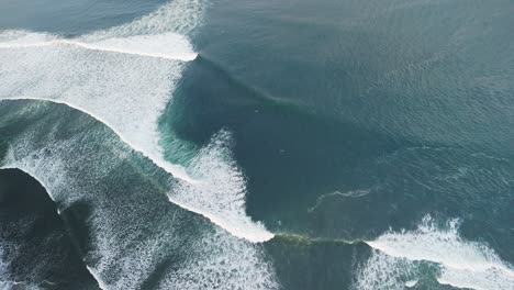 Bali-Surfer-Beach-Mit-Blaugrünen-Wellen,-Die-Entlang-Der-Küste-Anschwellen,-Mit-Winzigen-Surfern,-Die-Von-Der-Dünung-In-Den-Schatten-Gestellt-Werden