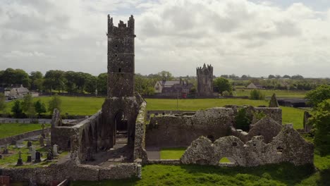 Blick-Von-Hinten-Auf-Das-Kloster-Claregalway-Mit-Der-Burg-In-Der-Ferne,-Drohnen-Dolly-über-Dem-Friedhof