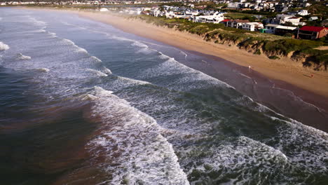 Drone-tilt-up-view-of-waves-crashing-onto-Lappiesbaai-sandy-beach-at-sunrise