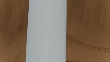 Close-Up-of-Propeller-Blade-from-a-Wind-Turbine-Looking-Down-with-an-Aerial-Drone,-Farmland-Fields-in-the-Background