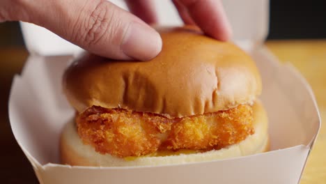 Hand-Legt-Ein-Brötchen-Auf-Ein-Knusprig-Gebratenes-Fischsandwich-Mit-Mayonnaise-Und-Käse-In-Einer-Fast-Food-Box