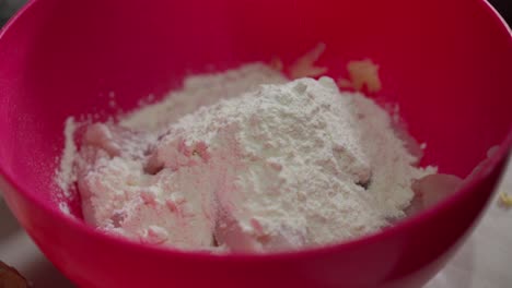 Chicken-being-coated-with-flour-in-a-red-bowl-for-cooking-preparation