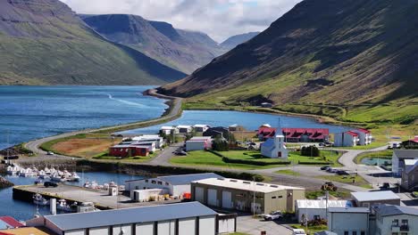 Aerial-View-of-Sudureyri-Fishing-Village,-Iceland-on-Sunny-Day,-Fjord,-Landscape,-Church-and-Buildings-60fps