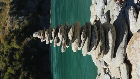 Stones-stacked-to-make-a-cairn-along-the-Kawarau-River,-South-Island-New-Zealand---vertical-parallax
