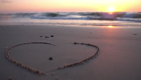 Heart-symbol-drawn-on-sand-against-a-backdrop-of-sunset-over-the-sea