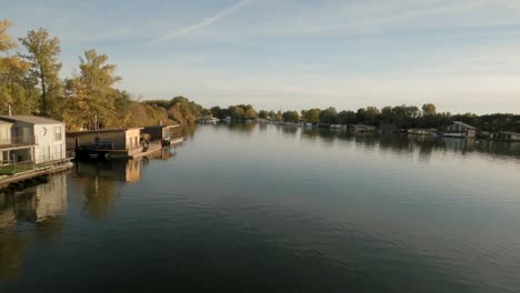 Drohnenaufnahmen-Zeigen-Einen-Ruhigen-Fluss-In-Mitteleuropa,-Gesäumt-Von-Hausbooten-Und-Herbstbäumen