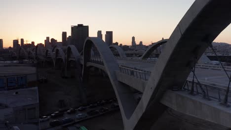 Aerial-low-tracking-shot-along-the-6th-Street-Bridge-and-Viaduct-in-downtown-Los-Angeles,-California-at-sunset