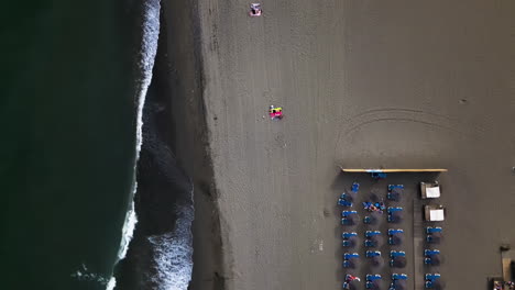 Foamy-ocean-waves-flowing-over-sandy-beach-with-sunbeds,-aerial-top-down-view