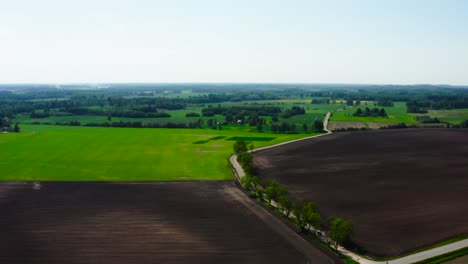 Luftaufnahme-Eines-Dunklen-Erdfeldes-Und-Grünen-Weizenackerlandes-Mit-Baumgrenze,-Lettland