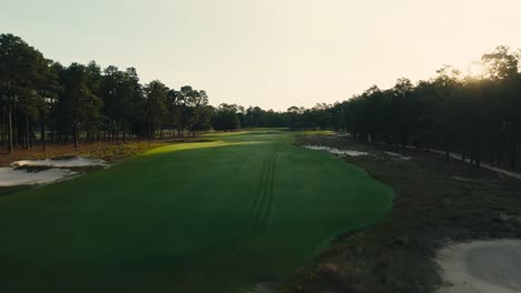drone-shot-down-the-fairway-at-a-golf-course-as-the-rising-sun-peaks-of-the-trees