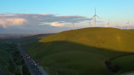 Drone-shot-of-a-sunlit-wind-turbines-and-a-highway,-sunset-in-San-Francisco,-USA
