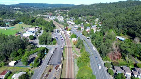 Landschaftsaufnahme-Von-Autos,-Die-Auf-Der-Hauptstraße-Der-Stadt-Fahren,-Mit-Bahnhof,-Eisenbahngeschäften,-Buschland,-Vororten,-Ourimbah,-Central-Coast,-Australien,-Drohnenluftaufnahme