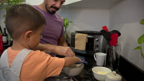 Slow-motion-of-a-mexican-latin-father-in-a-purple-shirt-making-cookies-with-his-son-sifting-flour-with-their-fingers-making-a-mess-in-the-kitchen