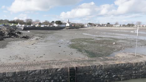 Reveal-of-Bordeaux-Harbour-Guernsey-at-low-tide-with-harbour-wall,-boats-drying-out-on-sand,beach-and-cottages-in-the-background-on-a-bright-day