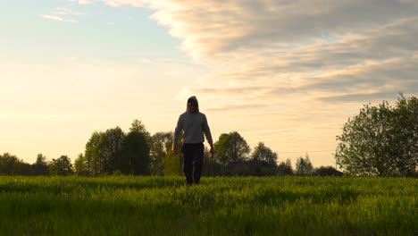 Farmer-walk-on-green-wheat-field-during-idyllic-golden-hour-sunset,-Latvia