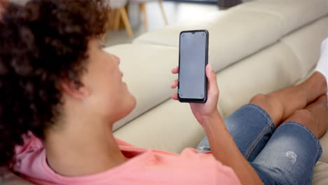 Eine-Junge-Person-Mit-Gemischter-Abstammung-Hält-Ein-Smartphone-Auf-Einem-Sofa-Zu-Hause