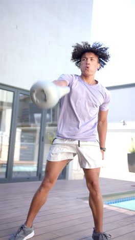 Vertical-video:-A-young-biracial-man-is-training-with-a-kettlebell-outdoors