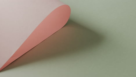 Close-up-of-pink-rolled-paper-on-pale-green-background-with-copy-space-in-slow-motion
