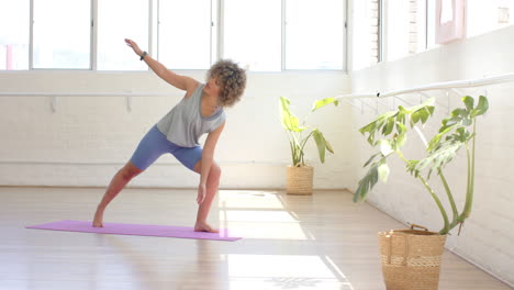 Biracial-young-woman-practicing-yoga-in-bright-studio