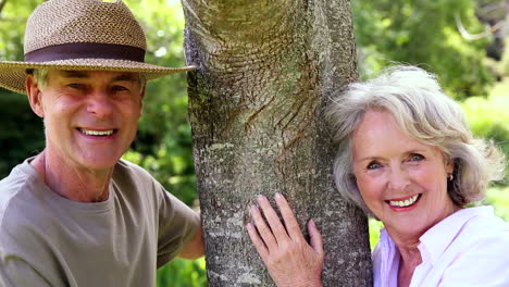 Retired-couple-leaning-against-tree-smiling-at-each-other