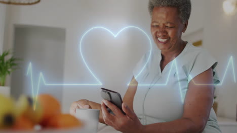Animation-of-heart-shape-cardiograph-over-senior-biracial-woman-using-smartphone