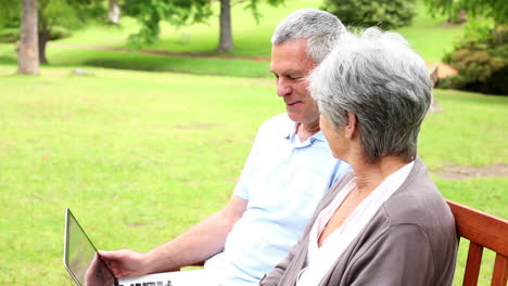 Retired-couple-sitting-on-a-park-bench-using-a-laptop