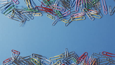 Colorful-paper-clips-are-scattered-across-a-blue-background,-with-copy-space