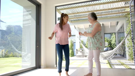 Asian-grandmother-and-biracial-granddaughter-dancing-on-patio