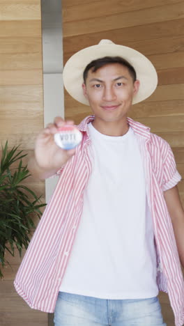 Vertical-video:-Asian-male-wearing-straw-hat-is-holding-up-a-VOTE-badge